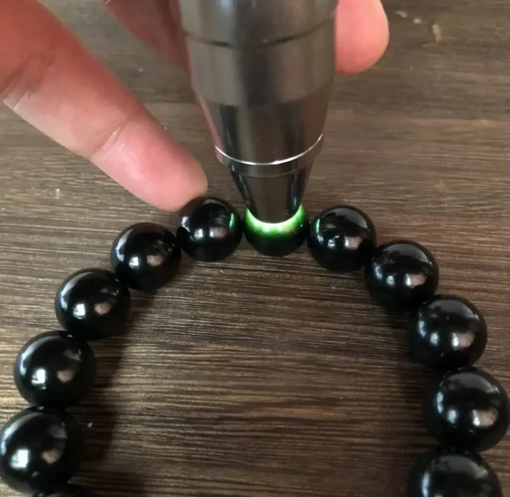 A 14mm Hei Qing jade bead reveals a greenish-grey base during a backlighting test.