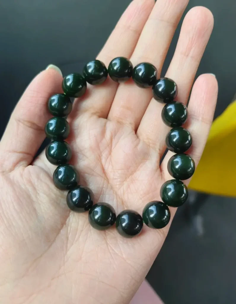 A 12mm Mo Biyu jade bead bracelet in a palm, showing a deep, jet-black lacquer-like appearance.