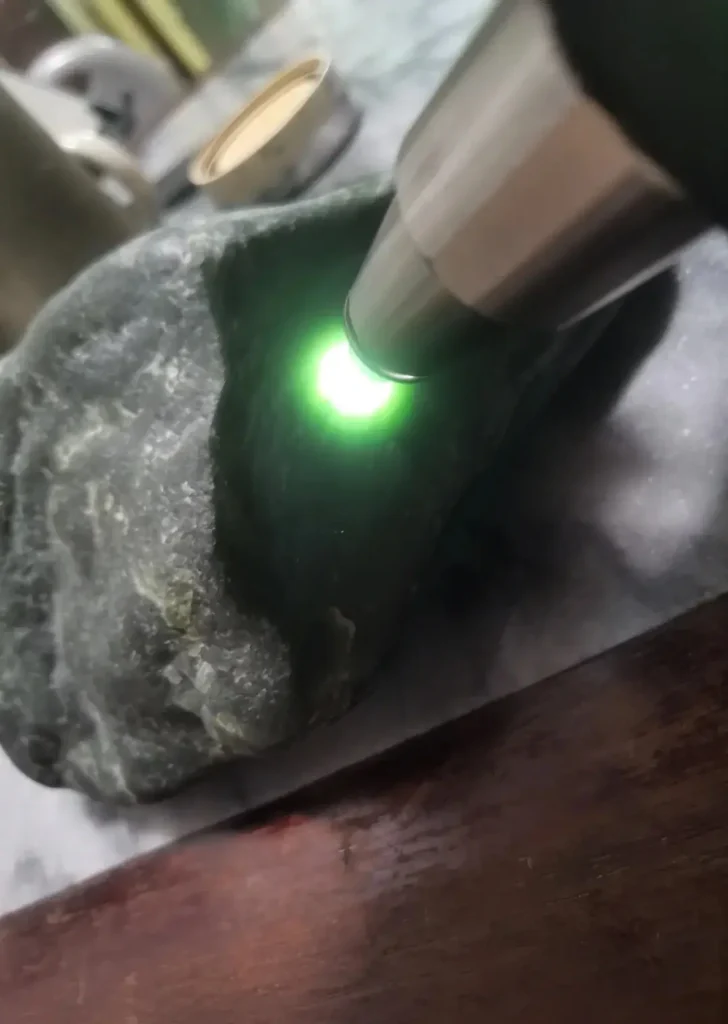 A dark Mo Biyu stone revealing a vibrant emerald green glow during a backlighting test.