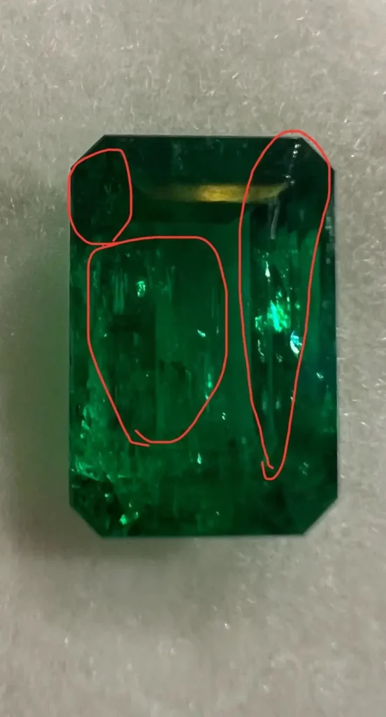 Red circles highlighting natural inclusions and internal fissures in a 1.1-carat emerald.