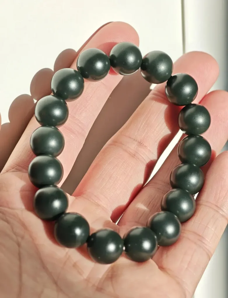 A hand holding a Taghma Black-Green Jade bracelet in natural light, showing an oily black luster.