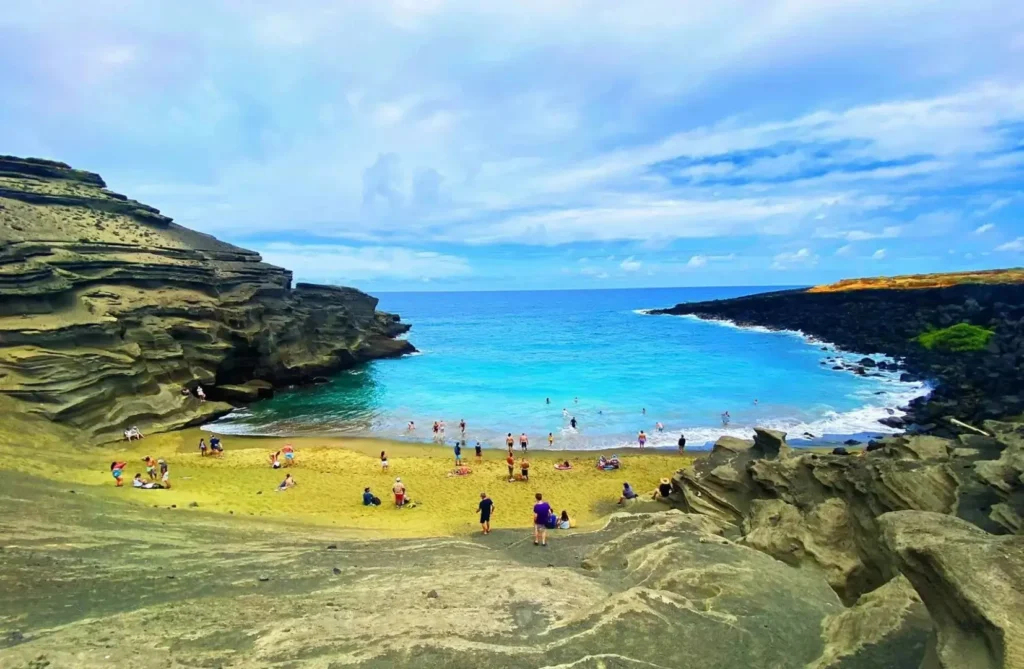 Visitors walking on the rare "matcha" green peridot sand and black rocks of Papakolea, Hawaii.