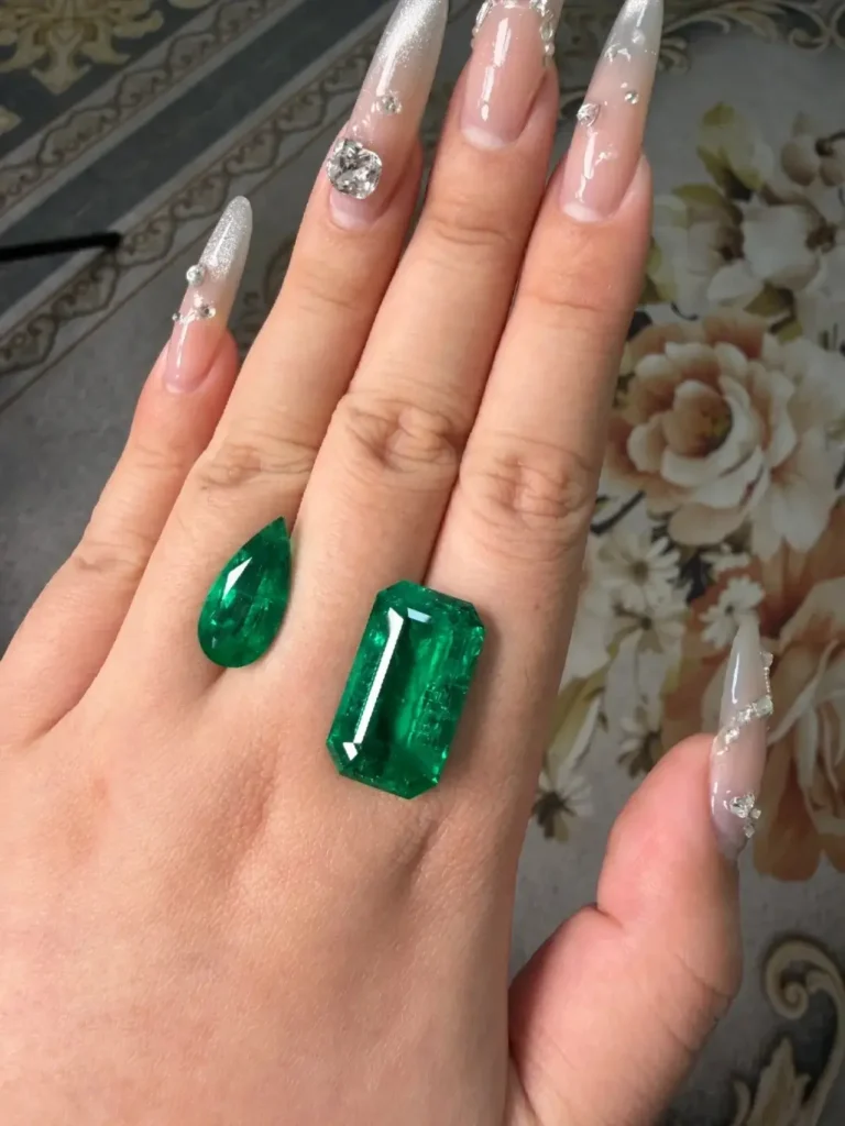 Pear-cut and emerald-cut loose emeralds displayed side-by-side for shape comparison.