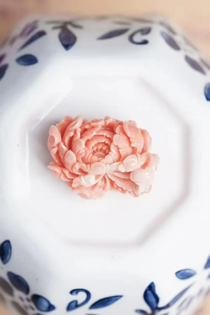 A hand-carved pink Momo coral peony pendant showing intricate, high-relief floral details.
