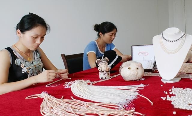 Wannian "Pearl Women" technicians sitting at a table skillfully stringing and assembling pearl jewelry.