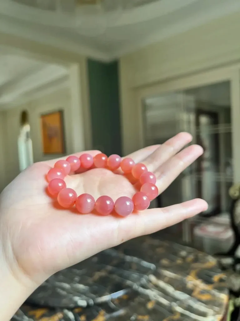 A strand of African Agate beads in a palm, showing a watery luster and pale red hues.