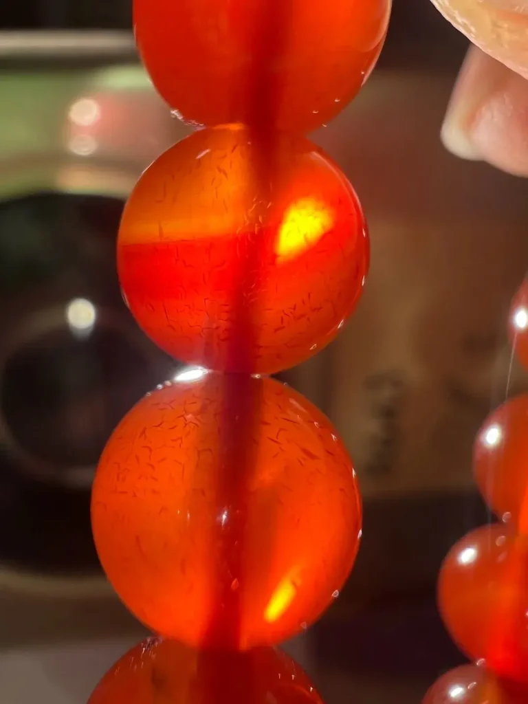 Backlit dyed agate bead showing fine dye-filled fractures and spider-web color lines.