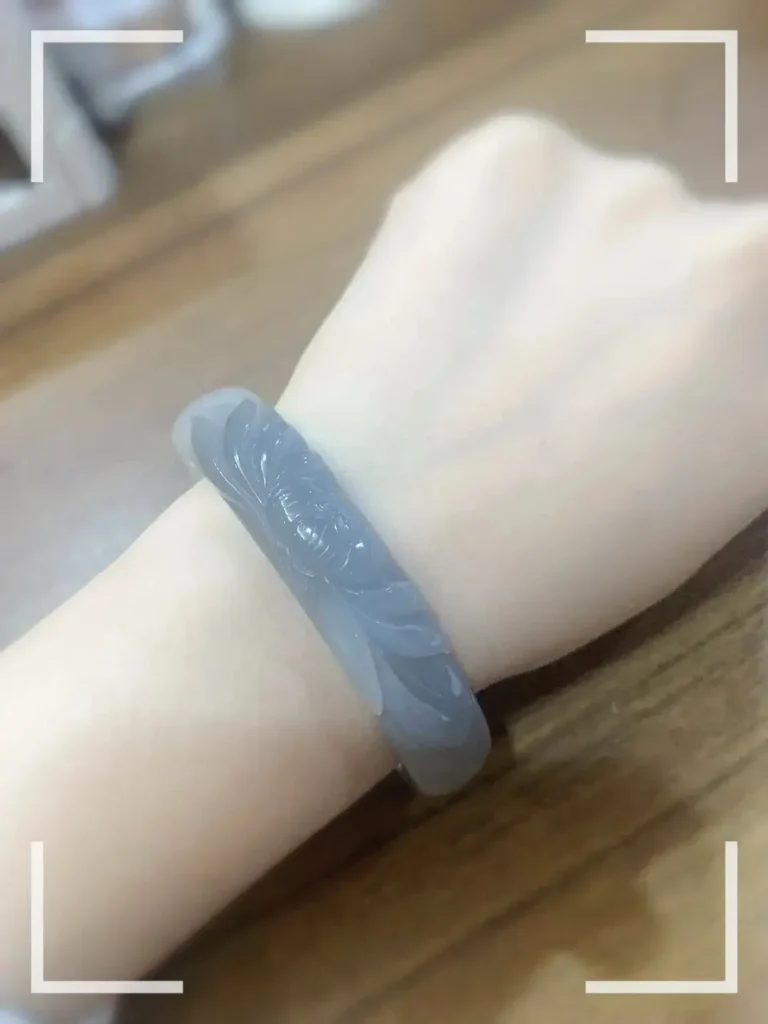 Smoky purple nephrite bangle on wrist, hand-carved with lotus and koi fish motifs in relief.