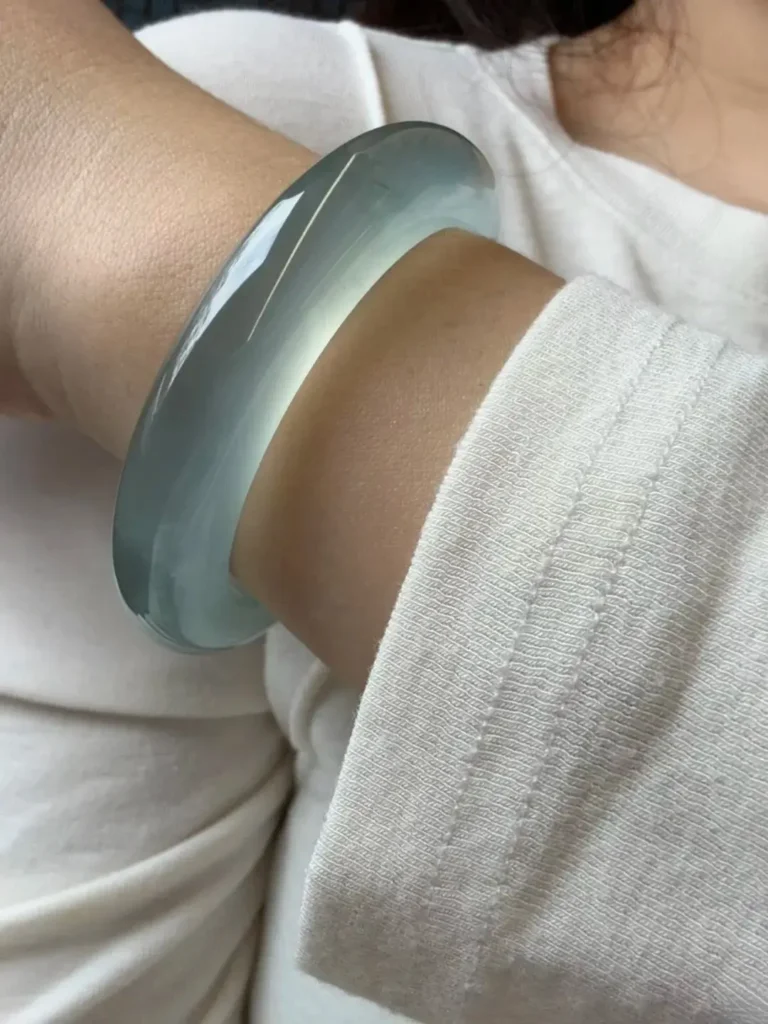 A person wearing a Blue Water jadeite bangle on their wrist in a natural, everyday setting.