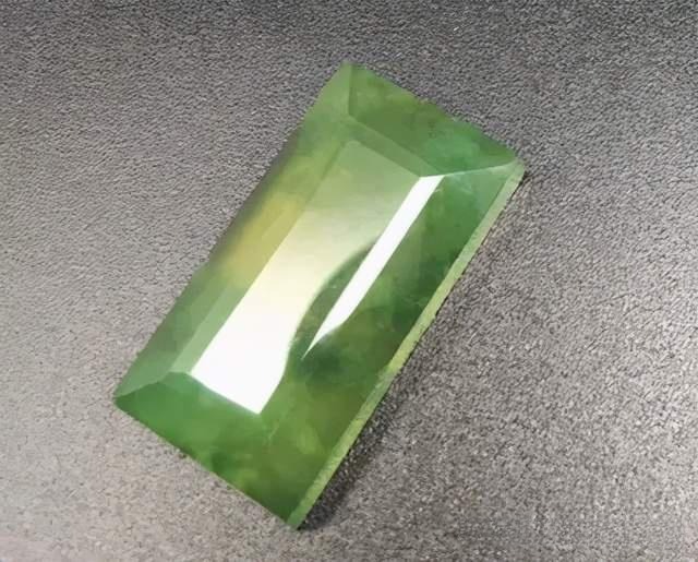 A faceted yellow-green Jin Cui Yu gemstone showing exceptional clarity and sharp geometric cuts.