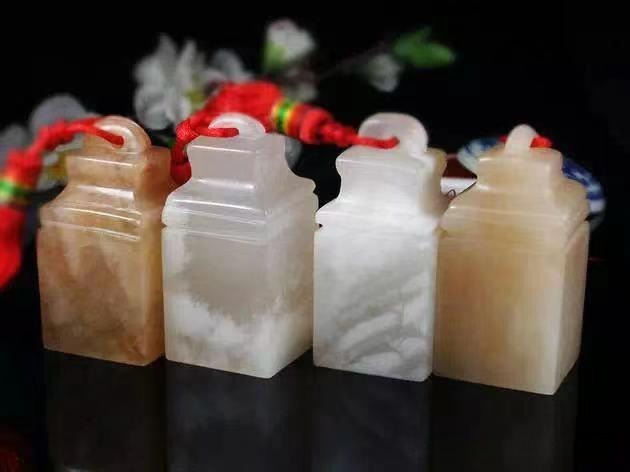 Four Xining Alabaster seals arranged side-by-side, showing diverse colors and translucent textures.