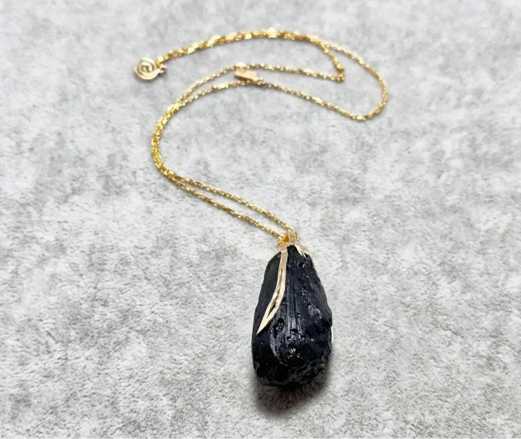 18K gold necklace with a polished black Hainan tektite pendant, showing a smooth and muted luster.