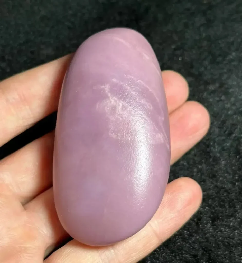 A hand holding a polished pink Anthophyllite Jade stone with vibrant lavender tones.
