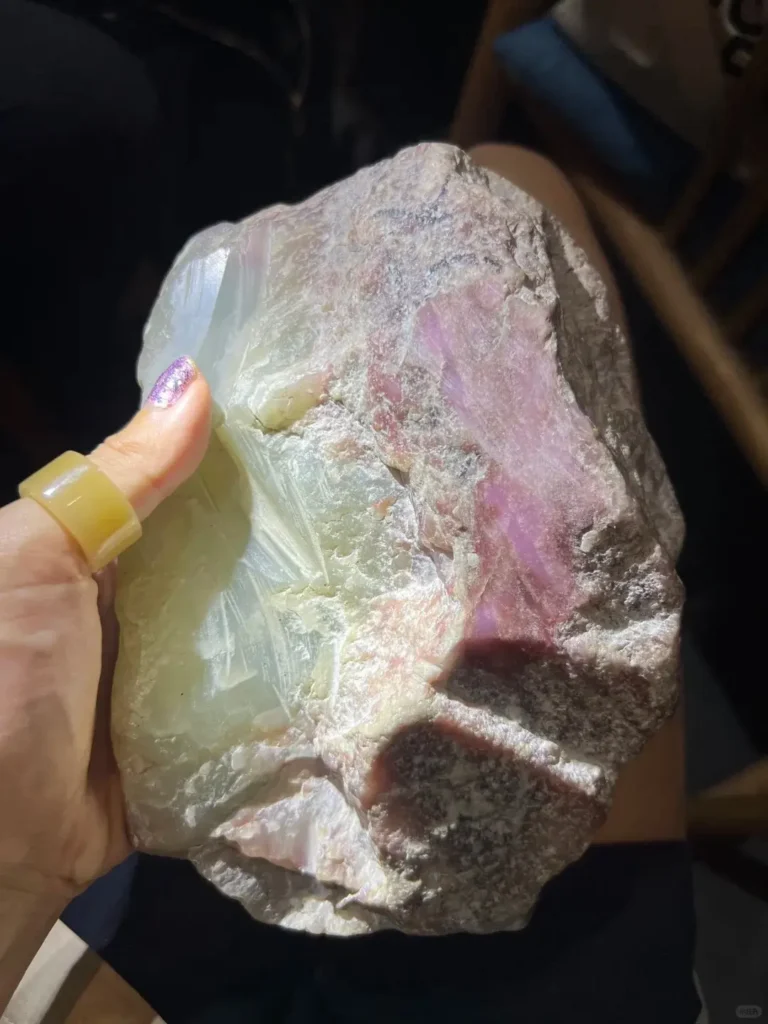 Hand holding a raw Anthophyllite stone showing faint pink hues through its translucent edges.
