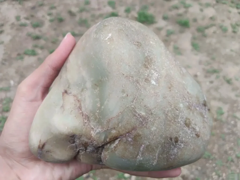 A large handheld Tremolite stone with faint greenish-blue hues appearing through its waxy surface.