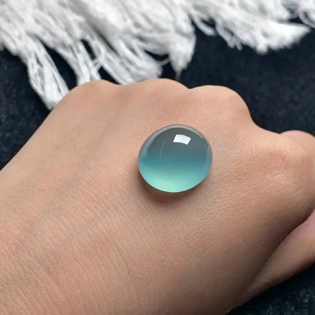 A high-ice grade Blue Water jadeite cabochon on a hand, exhibiting sharp crystalline rigidity.