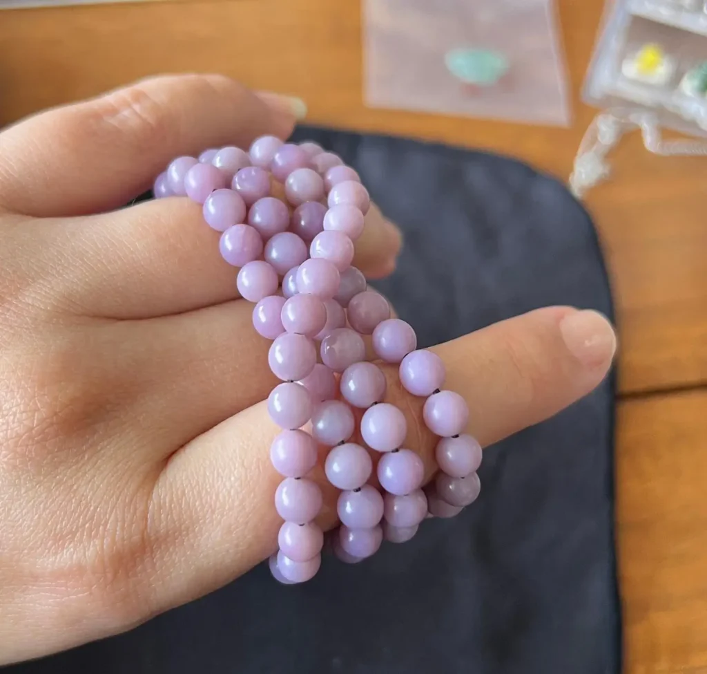 Close-up of a hand holding a taro purple Hetian jade bead strand for visual inspection.