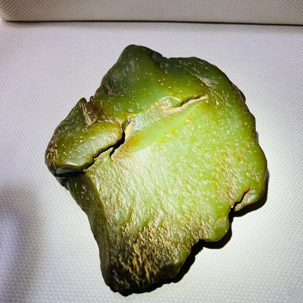 Light green Ximu Jade raw stone with fine texture and yellowish-brown skin spots.