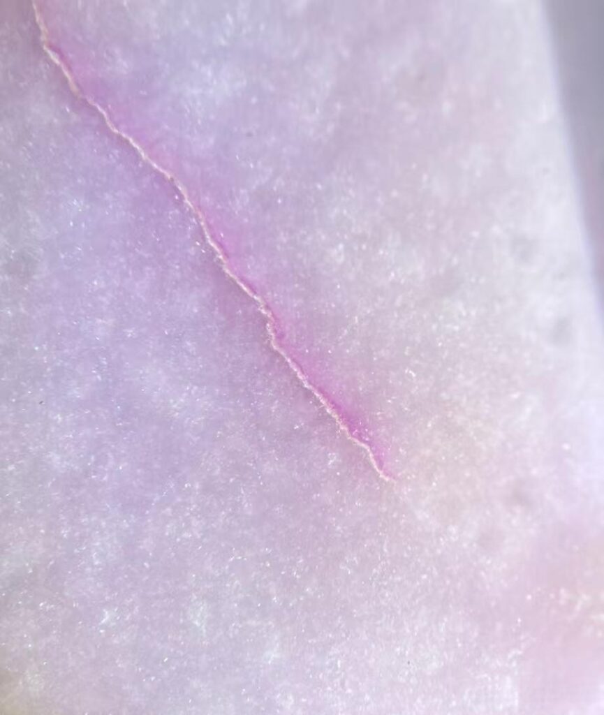 Microscopic view of purple pigment accumulation within the dense surface fractures of Hetian jade.