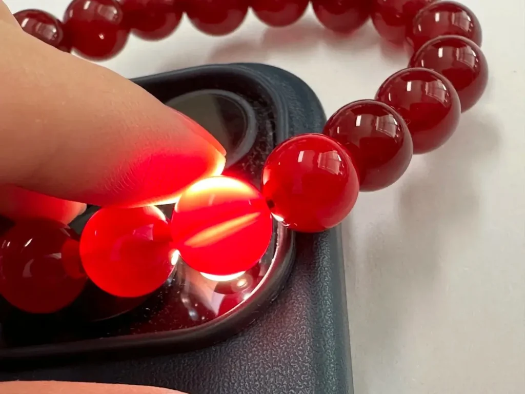 Dyed red agate beads under phone light, showing dye streaks and spider-web color patterns.