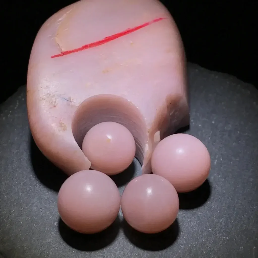 A pink raw stone next to a polished pink round bead showing uniform lavender hues.