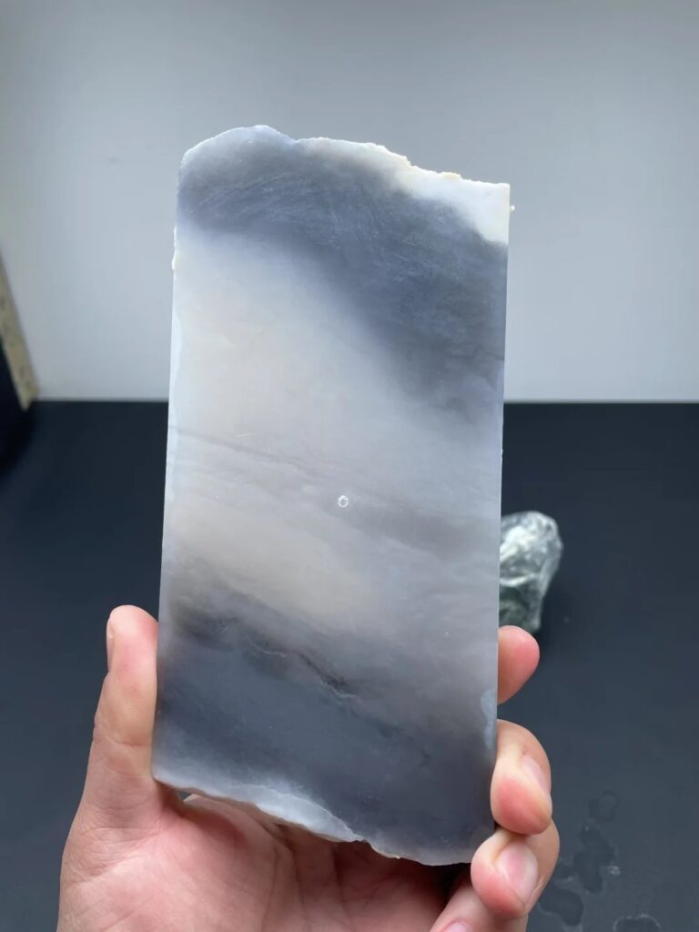 Hand holding a polished smoky purple nephrite specimen with a smooth surface and rich violet hue.