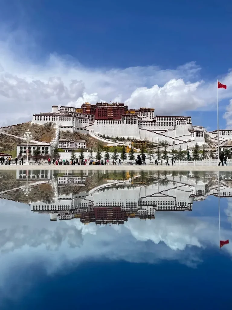 The Potala Palace reflected in a pool of water at the square under a clear blue Tibetan sky.