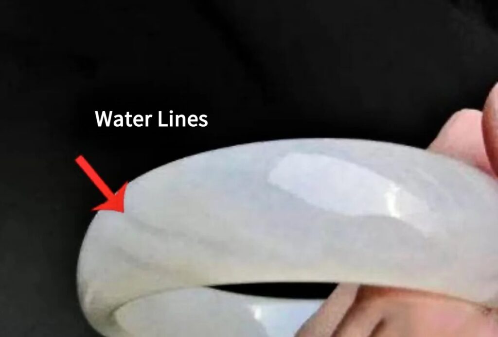 A Qinghai nephrite jade bracelet with a red arrow pointing to a visible transparent water line.