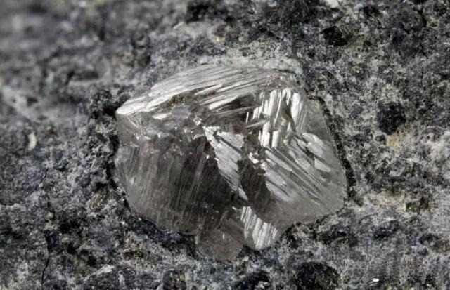 A large, transparent raw diamond crystal showing octahedral shape embedded in host matrix rock.