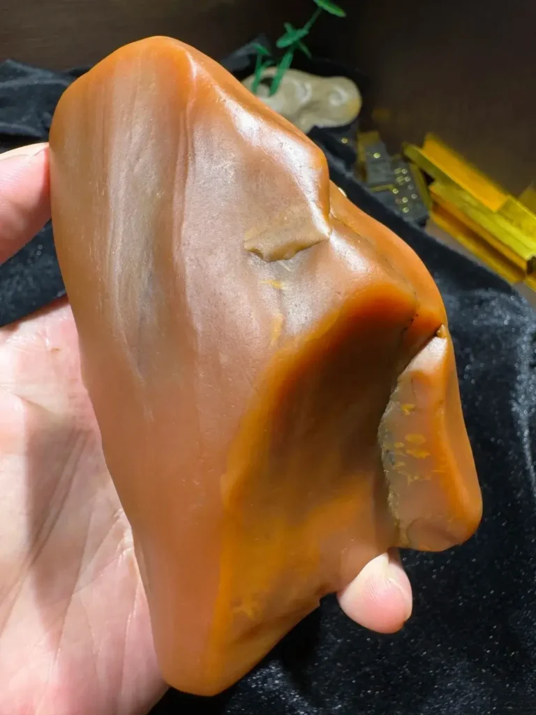 Hand-held raw Taishan Jade from Guangdong showing its natural waxy luster and golden-yellow hue.