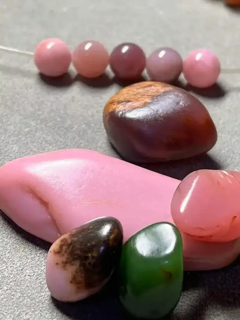 Several small raw pink Anthophyllite stones scattered with polished lavender-pink round beads.