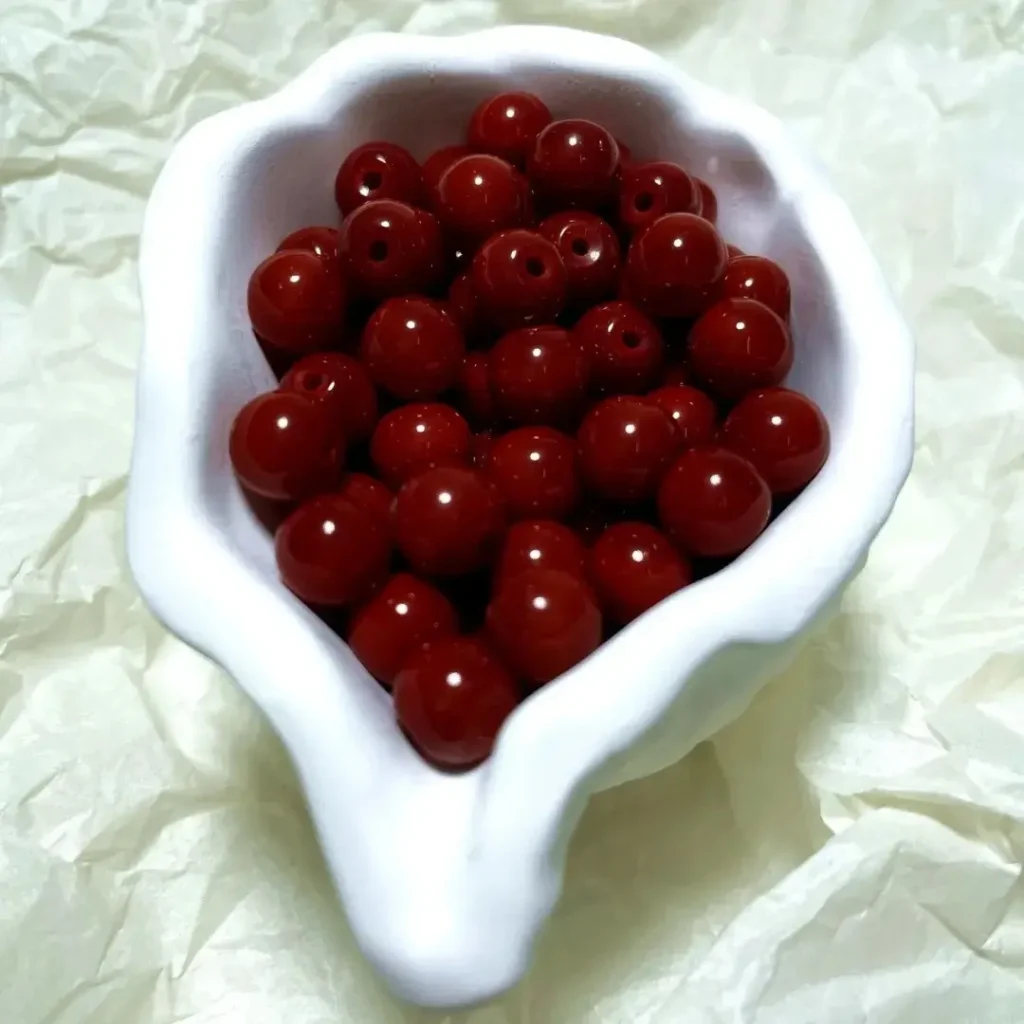 Red glass beads in a white ceramic bowl, showing uniform saturation and high surface luster.