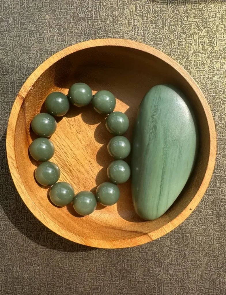 A raw Sha-zao-qing jade seed and a bead bracelet resting in a rustic wooden bowl.