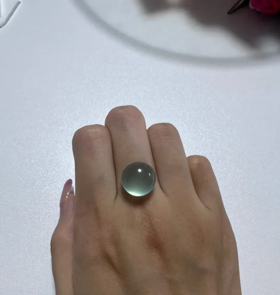 A translucent blue Tianqingdong cabochon held on the back of a hand under natural light.