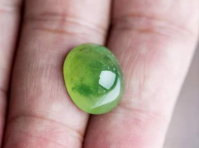 A yellow-green Vesuvianite Jade cabochon on a finger, displaying high clarity and vitreous luster.
