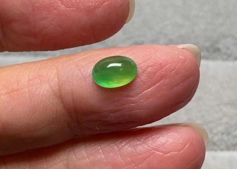 A vibrant yellow-green Jadeite cabochon held on a finger, showing high translucency and luster.