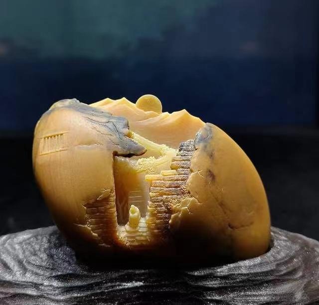 Exquisite Huanglong Jade carving featuring a miniature traditional village landscape and intricate textures.