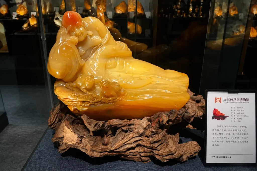 A honey-colored Huanglong Jade carving from Longling, Yunnan, exhibited on a natural wood base in a museum.