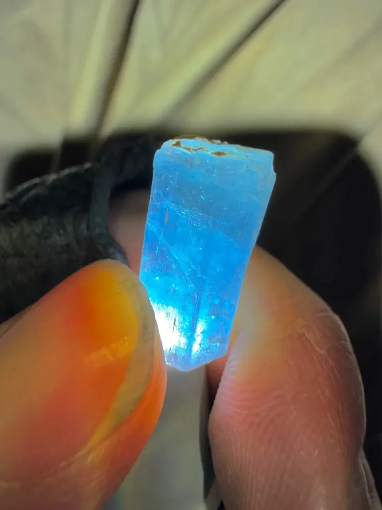 A hand-held aquamarine crystal from Yunnan showing natural liquid inclusions and internal fractures.