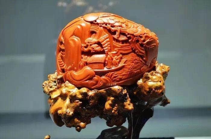 Intricate landscape carving on a reddish-orange Anhui yellow wax stone with a wooden base.