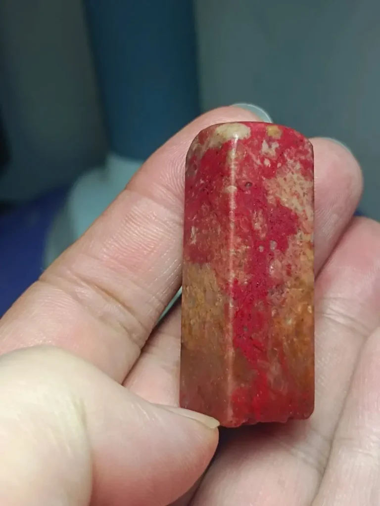 A hand holds an antique Zhejiang Changhua chicken-blood stone seal with red streaks on its faces and top.
