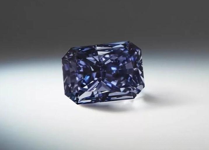 A radiant-cut diamond with a deep gray-violet hue resting on a gradient background.