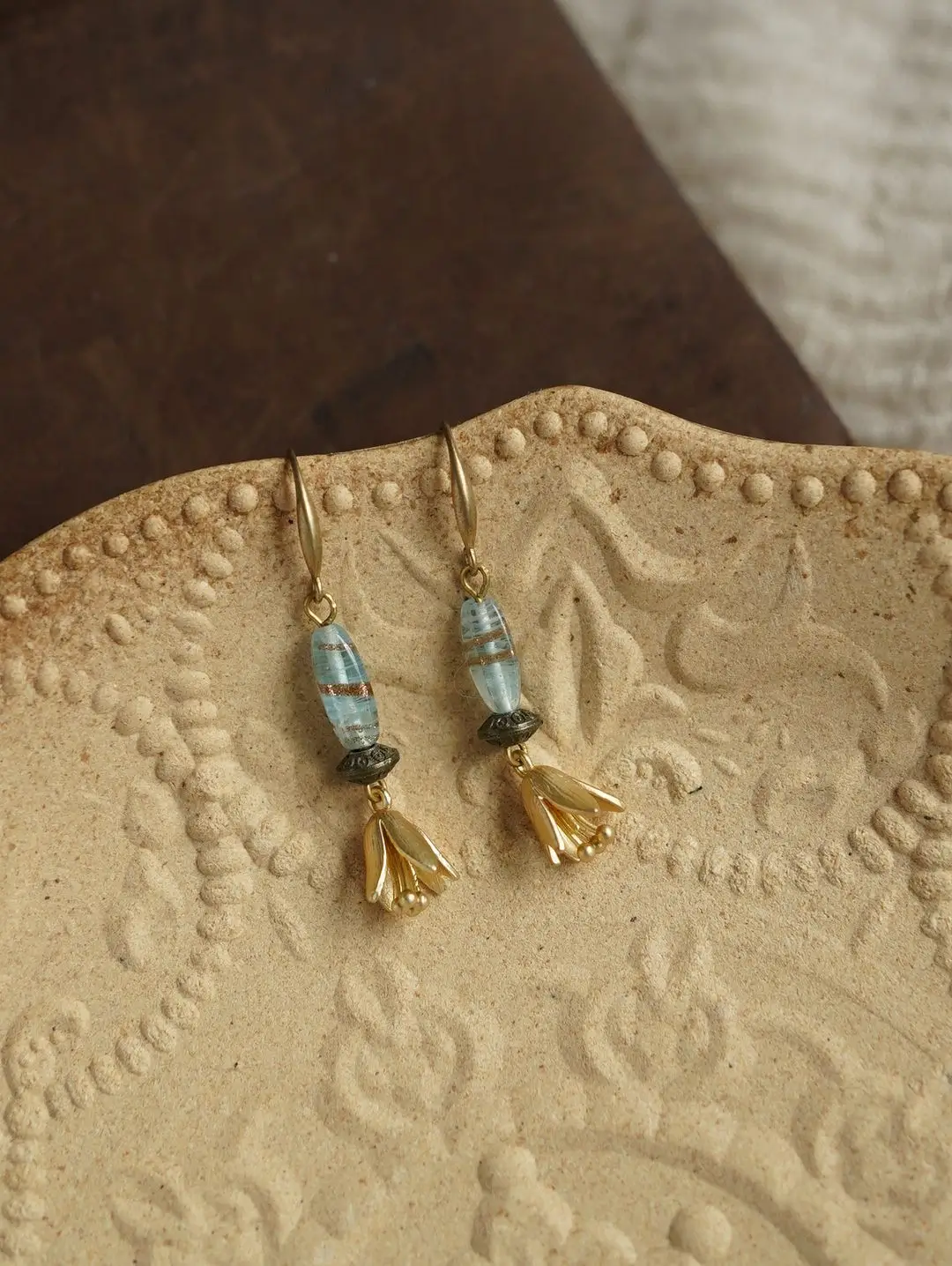Artisan jewelry resting on an embossed beige ceramic saucer with a dark wood background.