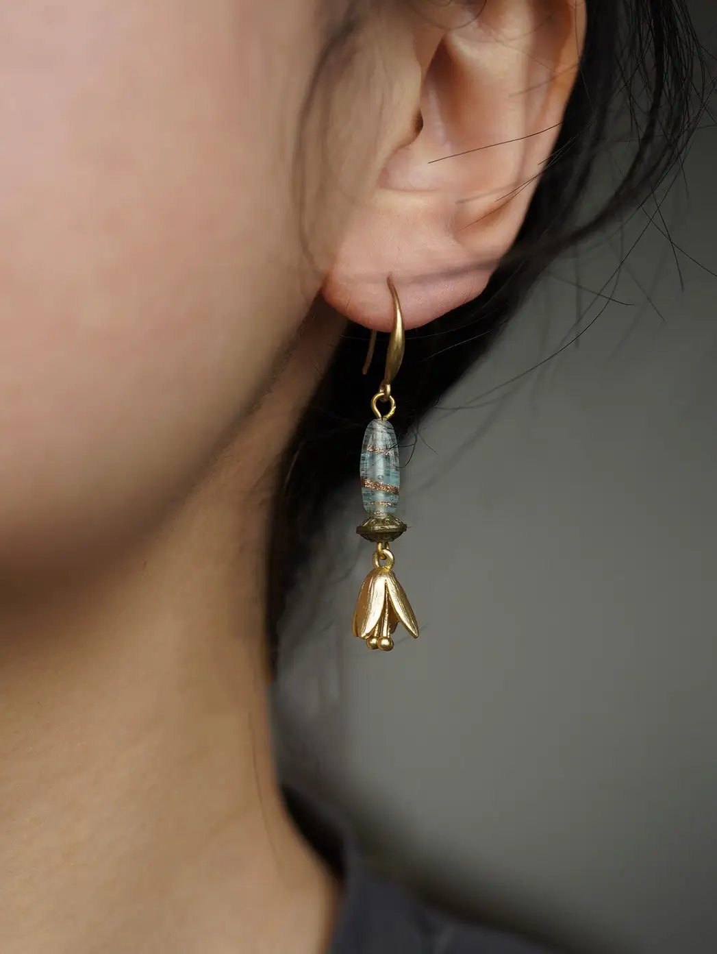 A botanical drop earring worn on a model's ear, showing the fit against a gray background.