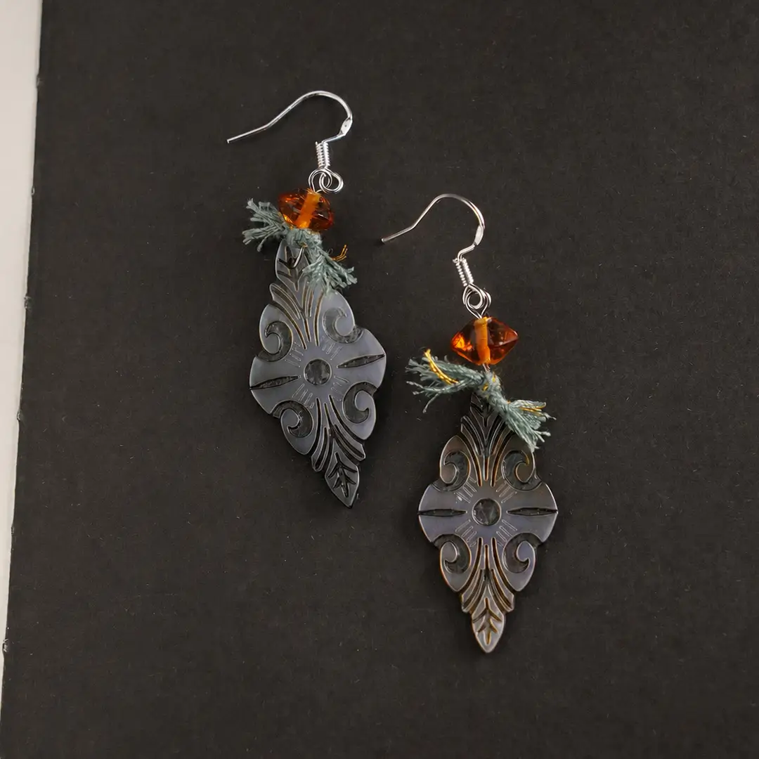 vintage-carved Black Mother of Pearl earrings with radiant orange glass on a black background.