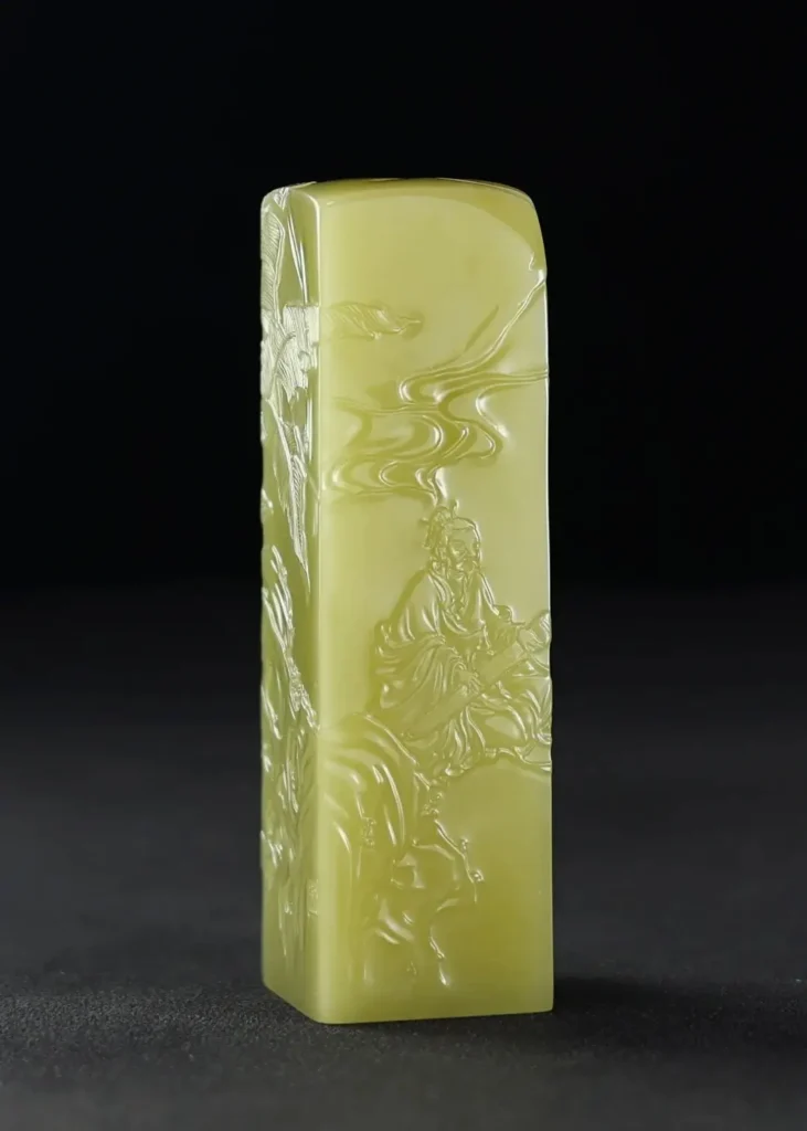 A light green Zhejiang Qingtian stone seal intricately carved with a traditional Chinese scholar figure.