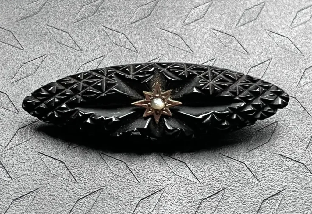 An elliptical Victorian mourning brooch with geometric carvings and a central gold star pearl.