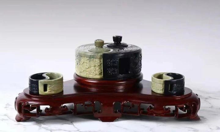 A Tai Chi ornament carved from yellowish-green and pure black jade on a wooden stand.