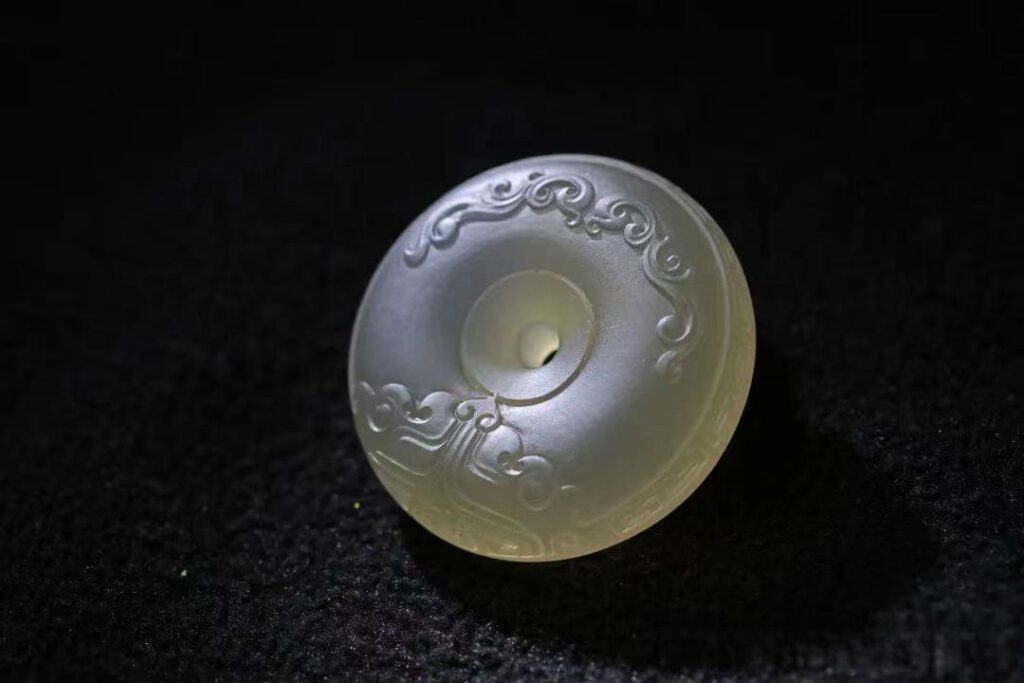 Carved white Shanxi Datong chalcedony pendant with traditional scroll patterns and a vitreous luster.