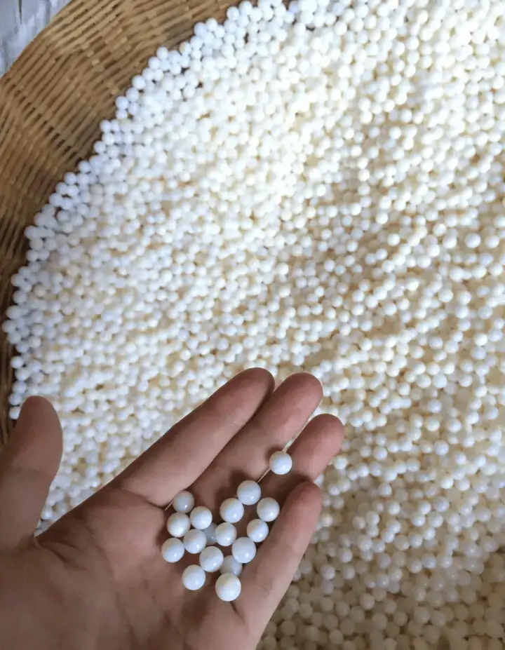 Round white shell bead nuclei for Edison pearl cultivation held in a hand over a basket.